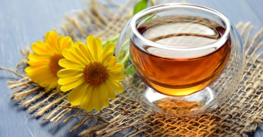 Glass cup of herbal tea with yellow flowers on a textured background.